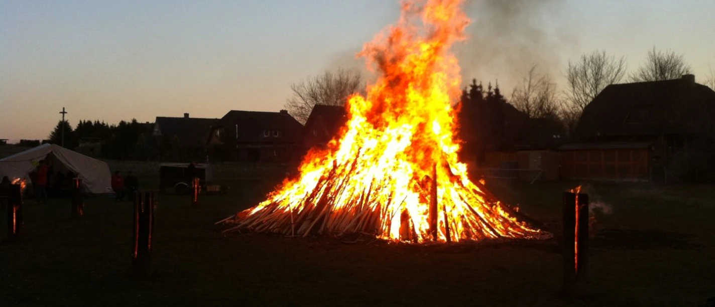osterfeuer-behringen Großes Osterfeuer leuchtet hell in der Dämmerung auf einer Wiese, umgeben von Schwedenfeuern.