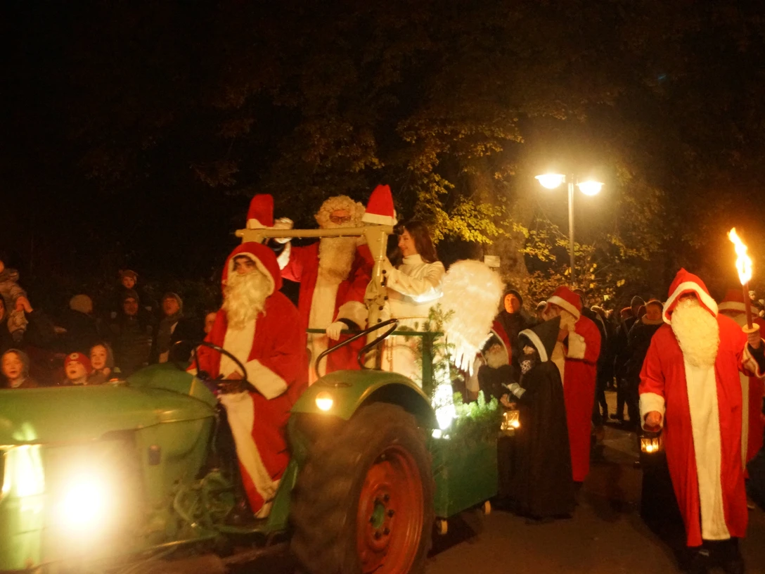 Weihnachtsmarkt 9.JPG Der Weihnachtsmann und zwei Begleiter auf einem Traktor, umgeben von Menschen bei Nacht.
