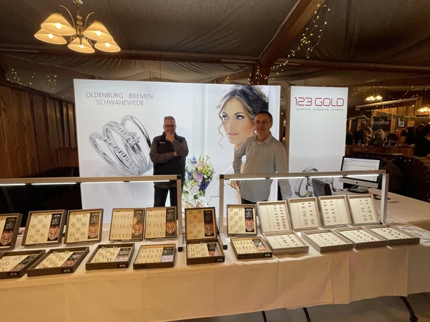 Messestand mit Schmuckauslage, zwei Personen präsentieren Ringe unter warmem Licht im Zelt.