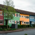 Reihenhäuser mit bunten Fassaden in Espelkamp. Grüne Sträucher und Bäume umrahmen die Szene.