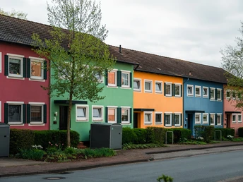 Reihenhäuser mit bunten Fassaden in Espelkamp. Grüne Sträucher und Bäume umrahmen die Szene.
