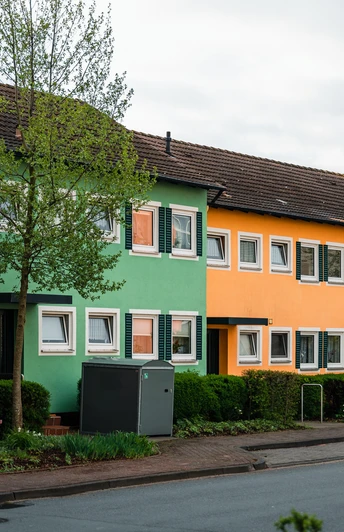 Reihenhäuser mit bunten Fassaden in Espelkamp. Grüne Sträucher und Bäume umrahmen die Szene.