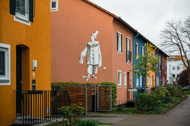 Espelkamp Reihenhäuser in bunten Farben, nachts ein Clown-Graffiti an einer orangefarbenen Hauswand.