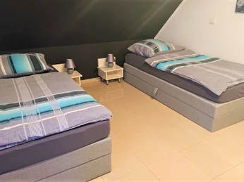 Zwei Einzelbetten mit gestreifter Bettwäsche in einem hell gefliesten Raum mit dunkler Deckenwand.