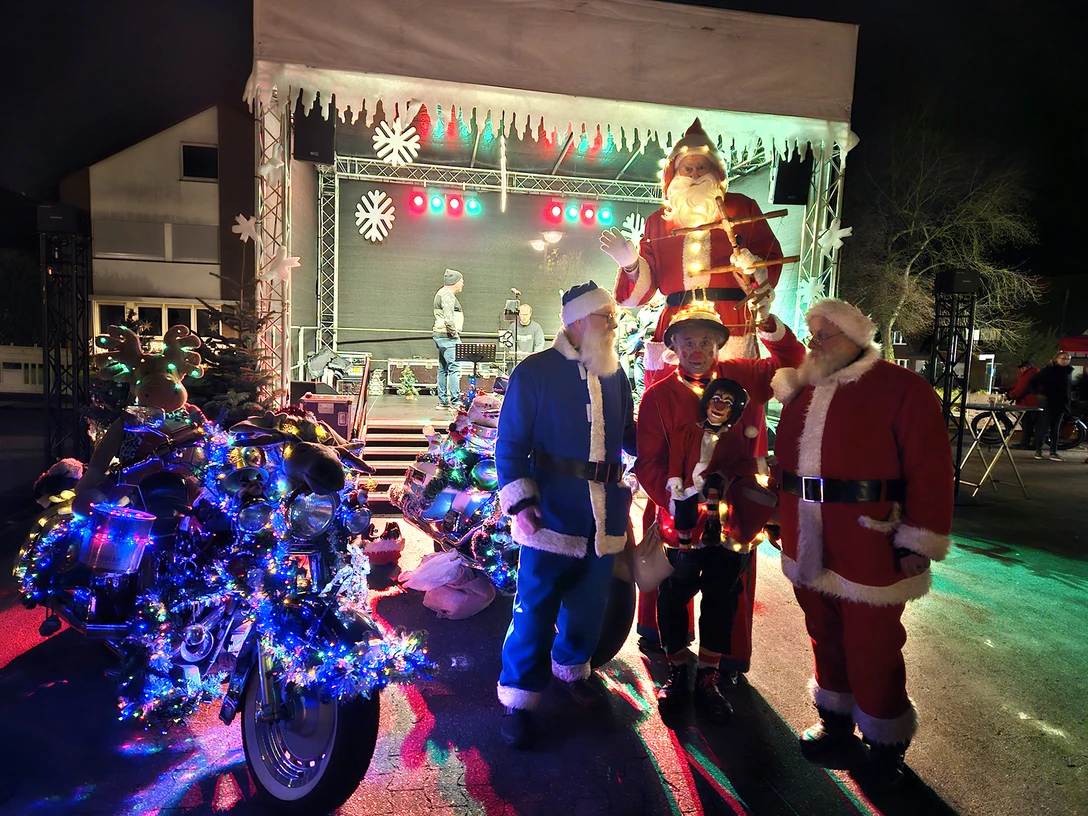 Fotos @ Pico Bello (1).jpg Weihnachtsmann-Darsteller posieren vor einer festlich beleuchteten Bühne mit Weihnachtsschmuck.