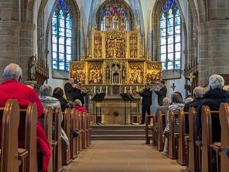 Drei Trompeter spielen vor einem goldenen Altar in der Propsteikirche St. Vitus in Meppen.
