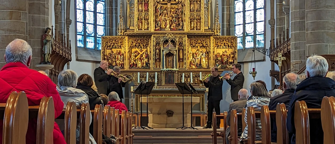 Drei Trompeter spielen vor einem goldenen Altar in der Propsteikirche St. Vitus in Meppen.