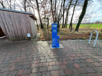 Radstation Mitte Niedersachsen Eine Fahrradstation mit Holzhütte und Feldern im Hintergrund, gelegen in einer ländlichen Umgebung.