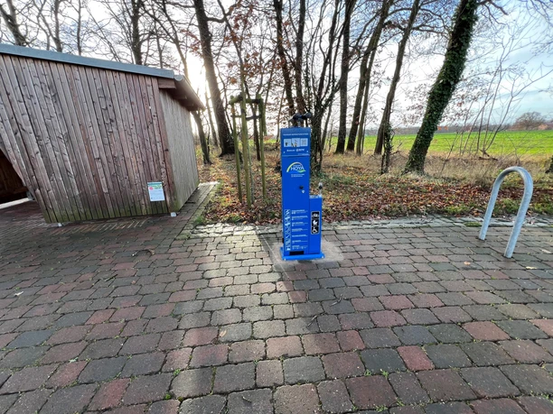 Radstation Mitte Niedersachsen Eine Fahrradstation mit Holzhütte und Feldern im Hintergrund, gelegen in einer ländlichen Umgebung.