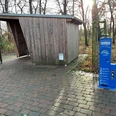 Radstation Mitte Niedersachsen Eine Fahrradstation mit blauer Reparatursäule steht auf einem gepflasterten Weg vor einem hölzernen Unterstand.