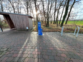 Radstation Mitte Niedersachsen Radstation mit Fahrradständern auf gepflastertem Platz, umgeben von Bäumen, im Hintergrund Wald.