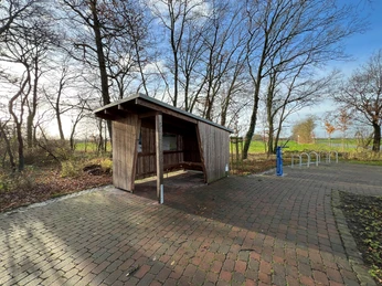 Radstation Mitte Niedersachsen Überdachter Rastplatz an einem Radweg mit Holzverkleidung, Fahrradständer und umgeben von Bäumen.