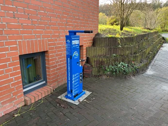 Radstation Hoyerhagen Fahrrad-Reparaturstation an einer Backsteinwand mit Werkzeugen. Ziegelmauerwerk und Grünanlage daneben.
