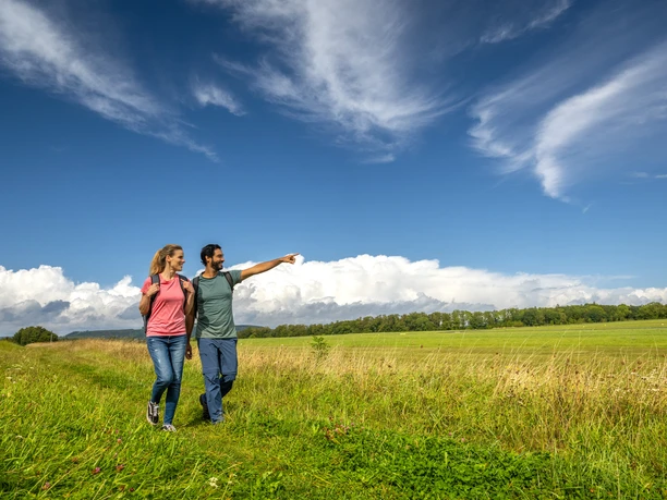 Couple walking across meadows with towering clouds in the background