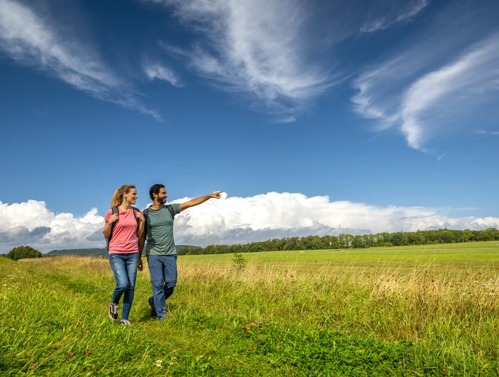 Über Wiesen wanderndes Pärchen mit hoch getürmten Wolken im HintergrundCouple walking across meadows with towering clouds in the background