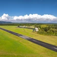 Aerial view of the runway surrounded by mown meadow and landscape with airport building and hangar on the right of the picture