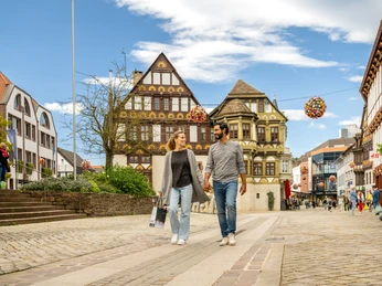 Fußgängerzone mit Menschen und flanierendem Pärchen vor der dem reich verzierten Fachwerkgebäude Dechanei Pedestrian zone with people and strolling couple in front of the richly decorated half-timbered building Dechanei