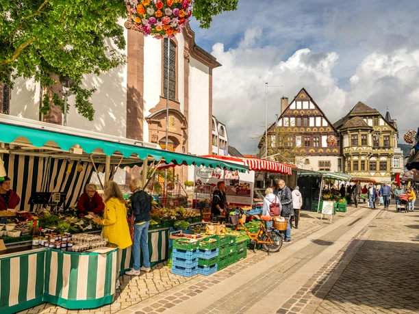 Weekly market with vegetable stalls in the pedestrian zone with shoppers and richly decorated half-timbered building in the background
