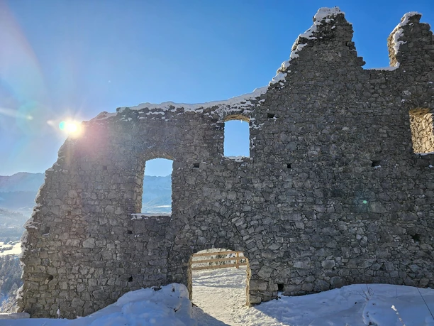 Burgruine Werdenfels im Winter Verschneite Burgruine mit Sonne über einer teils eingestürzten Steinmauer und Bergblick.