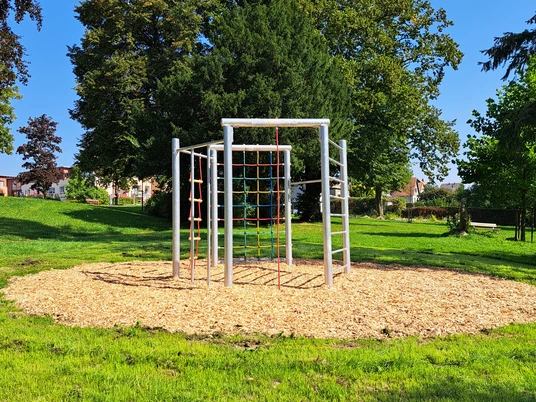 1_ParkMitPotential.jpg Geometrisches Klettergerüst in einem weitläufigen Park mit grüner Wiese und hohen Bäumen im Hintergrund.