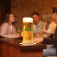 Barres Brauwelt - Frisch gezapft Ein frisch gezapftes Glas Bier steht im Vordergrund, mehrere Personen in geselliger Runde im Hintergrund.