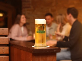 Barres Brauwelt - Frisch gezapft Ein frisch gezapftes Glas Bier steht im Vordergrund, mehrere Personen in geselliger Runde im Hintergrund.