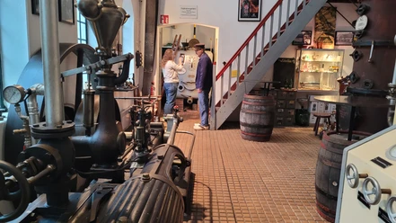 Alte Brennerei September Mitarbeiter in der Alten Brennerei September präsentieren historische Destillationsgeräte in einem Ausstellungsraum.