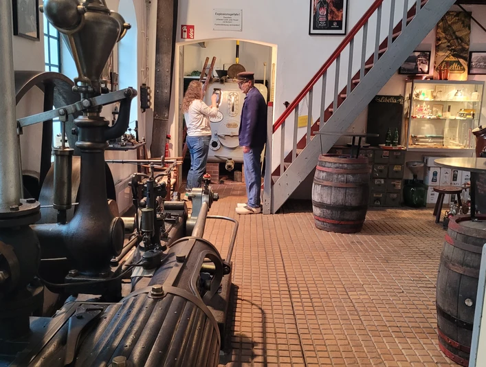 Alte Brennerei September Mitarbeiter in der Alten Brennerei September präsentieren historische Destillationsgeräte in einem Ausstellungsraum.