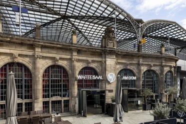 Wartesaal am Dom Historisches Gebäude mit prachtvollem Glasdach, davor Terrassenbereich; Aufschrift "Wartesaal".