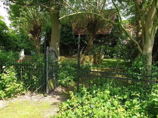 NaturGarten mit KunstObjekten -Gartentor zum alten Garten Metalltor im offenen Zustand eingerahmt von grünen Sträuchern, dahinter alter Garten mit Bäumen und Skulpturen.