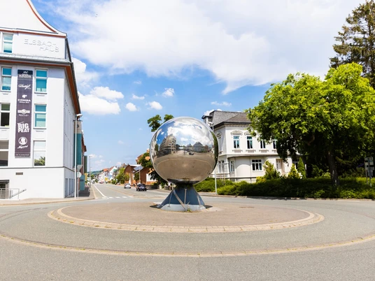 In einem modernen Stadtbild von Herford ragt eine große, glänzende Metallkugel in einem Kreisverkehr hervor.
