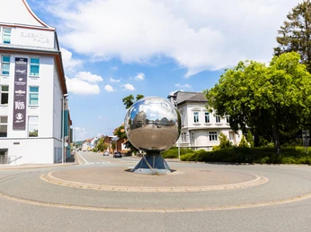 herford-marta-herford-teutoburger-wald-tourismus-h-tornow-032-cc-by-sa-jpg.jpg In einem modernen Stadtbild von Herford ragt eine große, glänzende Metallkugel in einem Kreisverkehr hervor.