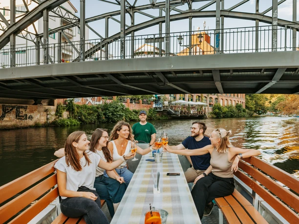 Bootstour auf der Weißen Elster - Wasserstadt Leipzig Eine Gruppe fährt mit einem Boot des Stadthafens Leipzig entlang der Weißen Elster, unter der Könneritzbrücke hindurch und stößt dabei mit einem erfrischenden Cocktail an, Wasserstadt Leipzig