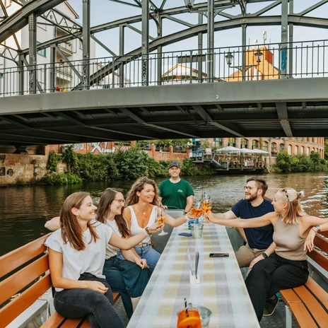 Skupina se plaví lodí z lipského přístavu po řece Weiße Elster pod mostem Könneritzbrücke a připíjí si osvěžujícím koktejlem, Water City Leipzig.
