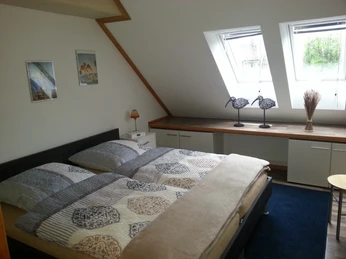 Doppelzimmer mit zwei Fenstern, modernem Doppelbett, blauem Teppich und dekorativen Bildern.