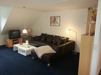 Modernes Wohnzimmer mit dunklem Ecksofa, weißem Couchtisch und Lampe auf blauem Teppichboden.