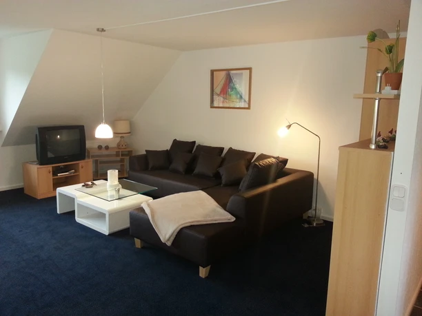 Modernes Wohnzimmer mit dunklem Ecksofa, weißem Couchtisch und Lampe auf blauem Teppichboden.