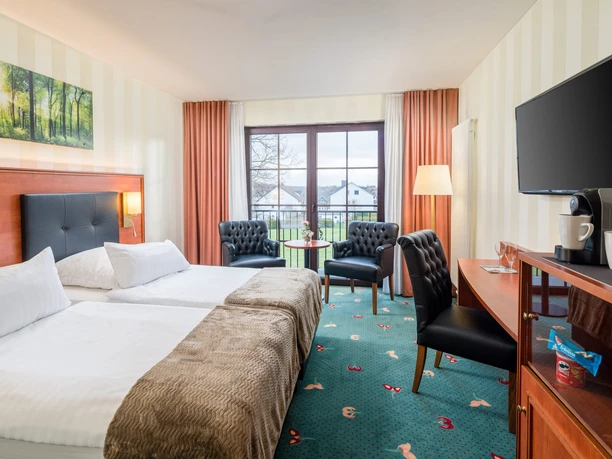 Hotel Freihof-Doppelzimmer.jpg Doppelzimmer mit großen Fenstern, modernen Möbeln, zwei Betten, einem TV und einem Schreibtisch.
