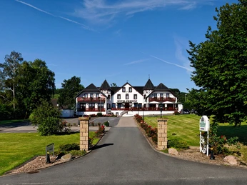 Breite Auffahrt führt zu einem imposanten Hotel mit Türmchen, umgeben von gepflegtem Grün.
