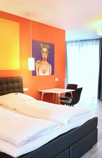 Helles Doppelzimmer mit modernem Design, Kunst an den Wänden, gemütlichen Sitzmöbeln und großem Fenster.