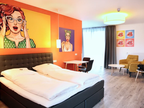 Helles Doppelzimmer mit modernem Design, Kunst an den Wänden, gemütlichen Sitzmöbeln und großem Fenster.