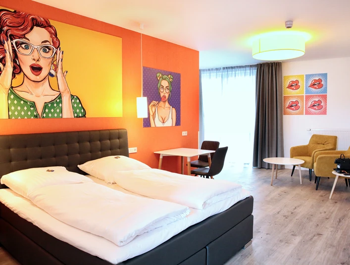 Helles Doppelzimmer mit modernem Design, Kunst an den Wänden, gemütlichen Sitzmöbeln und großem Fenster.