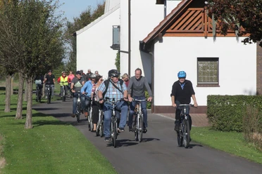 Stadtführer Espelkamp Radeln Radfahrergruppe auf asphaltiertem Weg durch ländliche Gegend, teils mit Helm und Freizeitkleidung.