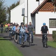Stadtführer Espelkamp Radeln Radfahrergruppe auf asphaltiertem Weg durch ländliche Gegend, teils mit Helm und Freizeitkleidung.