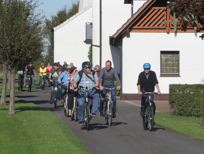 Stadtführer Espelkamp Radeln Radfahrergruppe auf asphaltiertem Weg durch ländliche Gegend, teils mit Helm und Freizeitkleidung.
