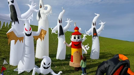 Drachenfest 2023 Ein Leuchtturm-Maskottchen posiert mit einem Kind vor großen, aufblasbaren Geister-Figuren.