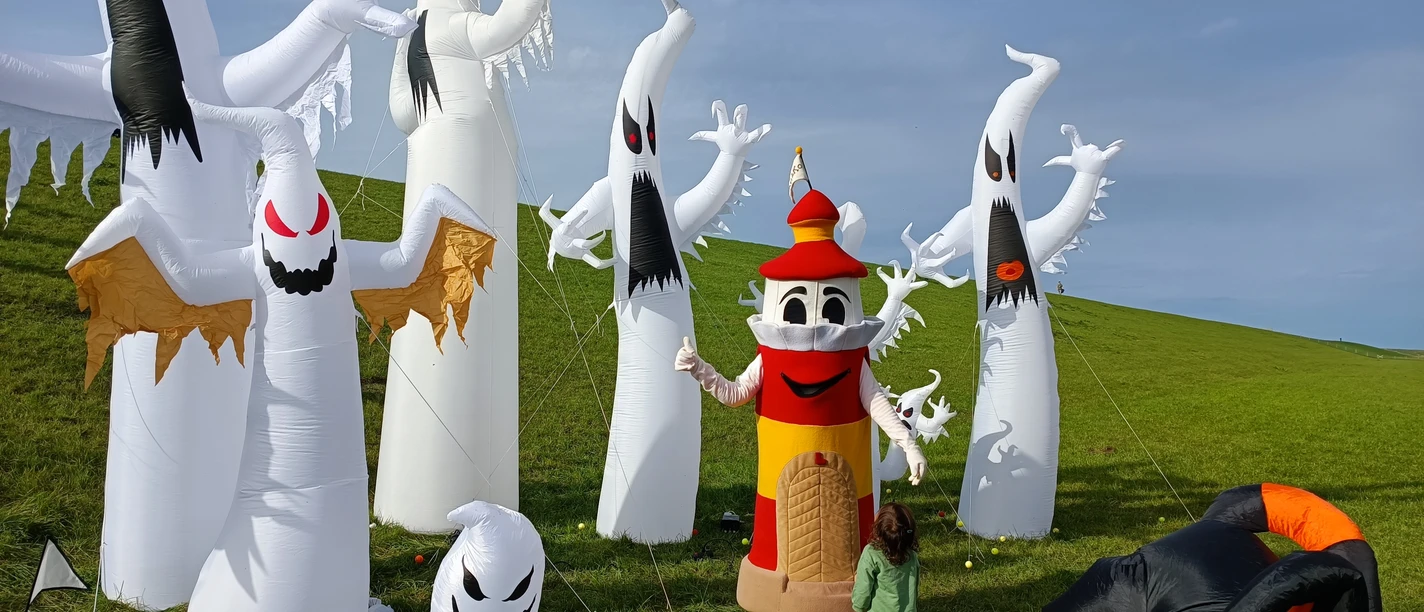 Drachenfest 2023 Ein Leuchtturm-Maskottchen posiert mit einem Kind vor großen, aufblasbaren Geister-Figuren.