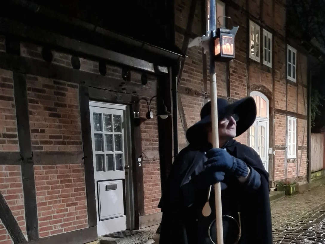Nachtwächter Ein Nachtwächter in historischem Gewand mit Laterne steht auf einem Kopfsteinpflaster vor Fachwerkhäusern.