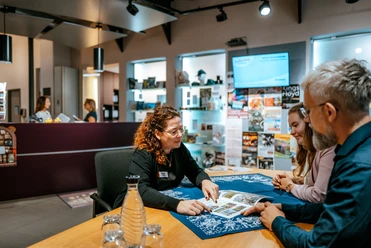Tourist-Information Mitarbeiterin berät zwei Gäste an einem Tisch in der Tourist-Information Einbeck.