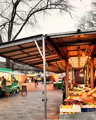Obst- und Gemüsestände auf einem typischen Wochenmarkt bei Tageslicht mit Besuchern.